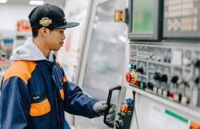Työhaalariin pukeutunut koneistajaopiskelija pitää kiinni CNC-koneen kahvasta.