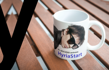 Pöydällä muki, jossa Cledos-artistin kuva ja teksti HyriaStart 21.-22.6.2022 verkossa