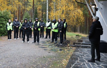 Mustiin haalareihin pukeutuneita ihmisiä ulkona rakennuksen edessä.
