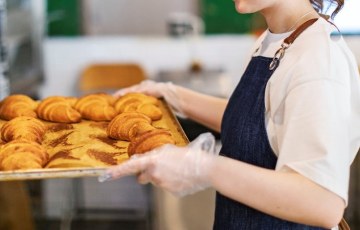 nainen laittaa croisantteja täynnä olevaa uunipeltiä kärryyn