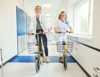 Kaksi terveysalan ammattilaista potkupyöräilemässä käytävässä, Kuva: Keski-Uudenmaan sote-TKIO -kuva Kuvaaja Iiro Rautiainen
