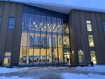 Kolmikerroksisen modernin puurakennuksen sisäänkäynti ulkoa isoine ikkunoineen.